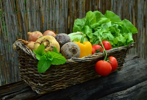 woven basket filled with fresh vegetables on a weathered wooden table