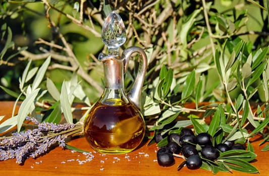 small vessel of oilive oil next to olives and olive tree vegetation